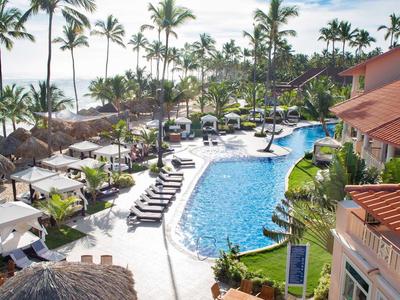 Výhled na tropický hotelový bazén s palmami, lehátky a slunečníky.