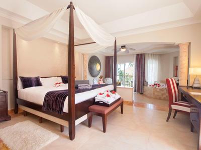 Jasny pokój hotelowy z łóżkiem baldachimowym, dużym lustrem i częścią wypoczynkową z biurkiem.