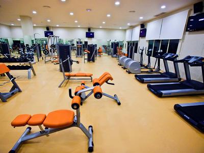 Moderní posilovna s různými cvičebními stroji a běžeckými pásy v světlé místnosti.