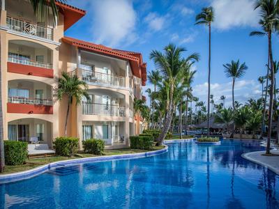 Hotelová budova s venkovním bazénem a palmami pod modrou oblohou.