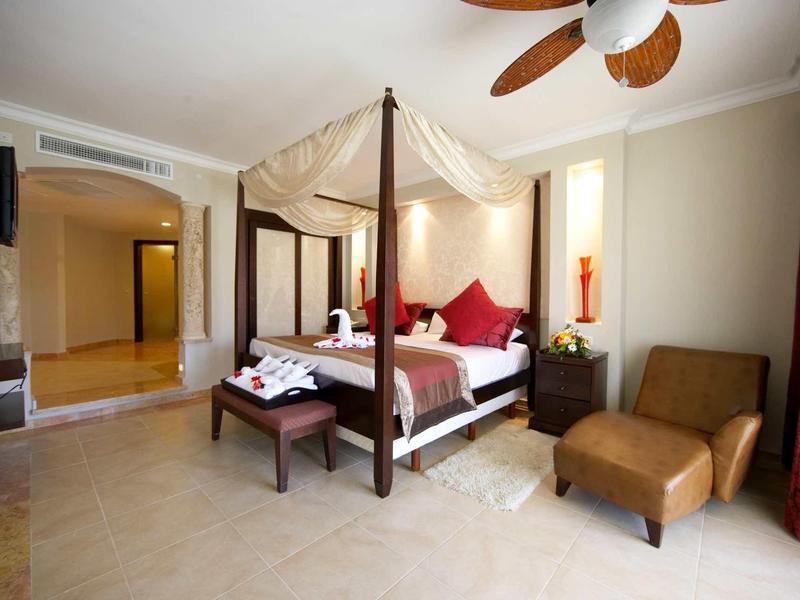 Elegancki pokój hotelowy z łożem z baldachimem, częścią wypoczynkową i ciepłymi kolorami.