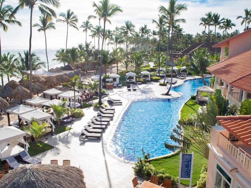 Widok na tropikalny basen hotelowy z palmami i parasolami nad morzem.