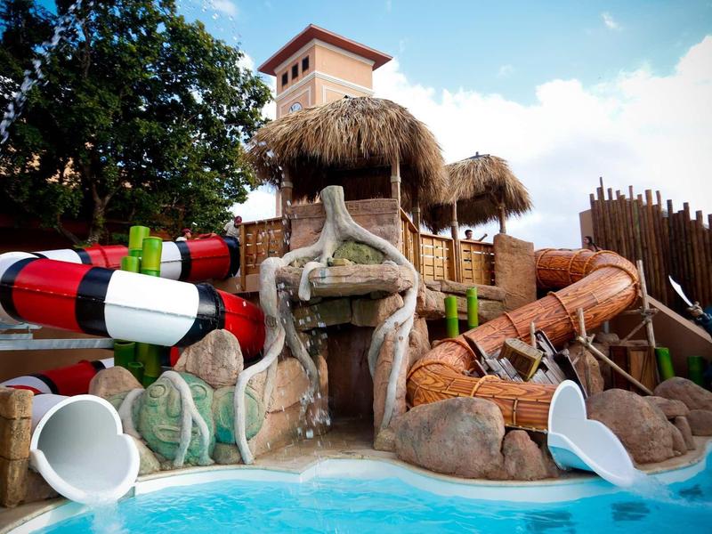 Kolorowy obszar zjeżdżalni wodnych z kamieniami i strzechą w basenie hotelowym.