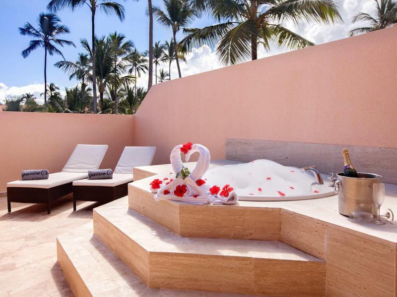 Jacuzzi z płatkami róż na tarasie z leżakami i palmami w tle.