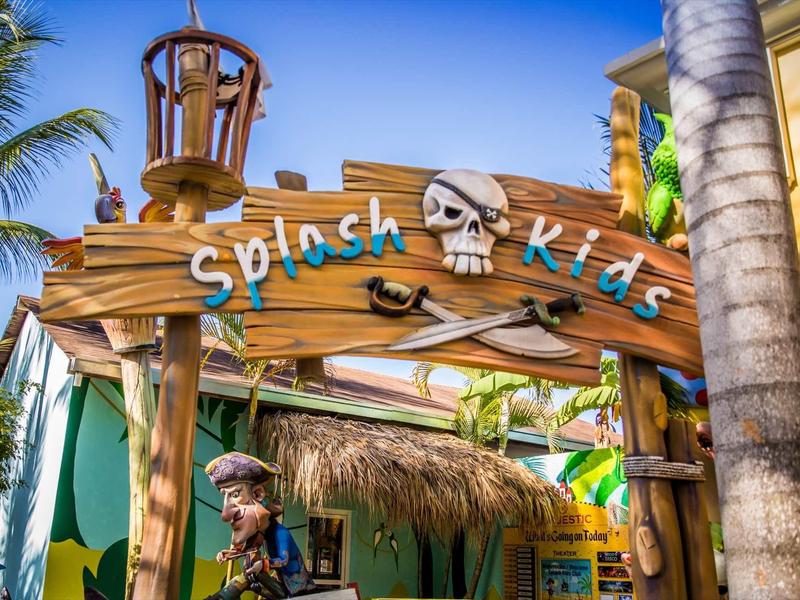 Kolorowe drewniane wejście do strefy wodnej Splash Kids z pirackimi dekoracjami i palmami.