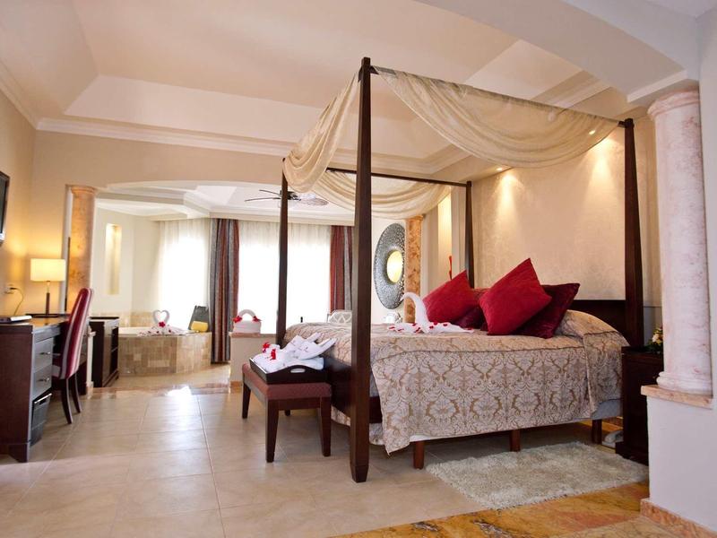 Elegancki pokój hotelowy z baldachimowym łóżkiem, czerwonymi akcentami i przytulnym kącikiem do siedzenia.