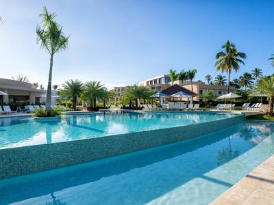 Luxuriöser Außenpool mit Palmen und Liegestühlen unter blauem Himmel in einer Hotelanlage.