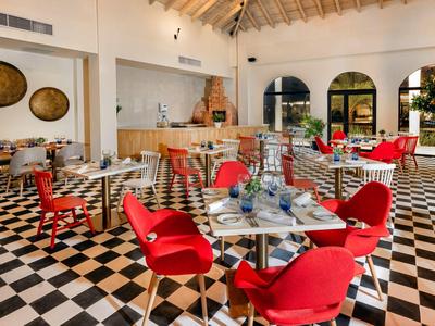 Ristorante moderno con pavimento a scacchi nero e bianco e sedie rosse sotto un soffitto con travi di legno chiaro.