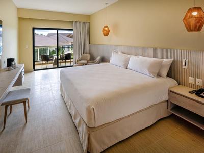 Camera d'hotel luminosa con letto grande, angolo salotto e balcone con vista mare.