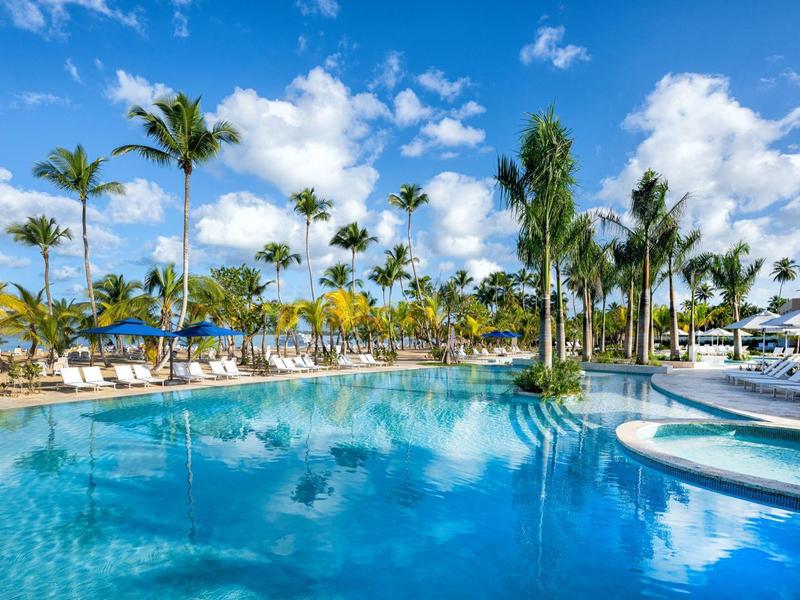 Grande piscina dell'hotel con palme, lettini e cielo azzurro.
