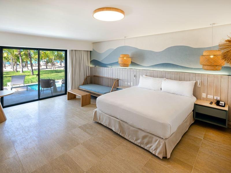 Camera d'hotel moderna con letto matrimoniale, vista sulla terrazza e sul giardino attraverso grandi finestre di vetro.