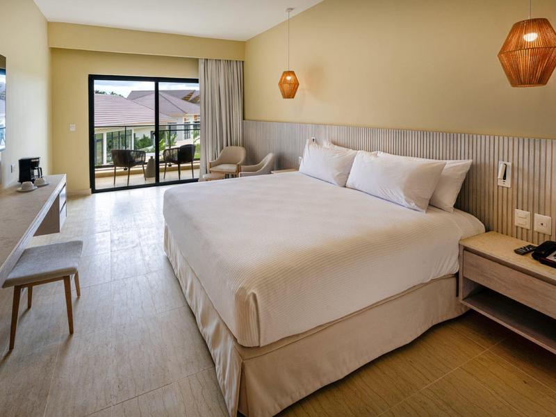 Camera d'hotel luminosa con letto grande, angolo salotto e balcone con vista mare.