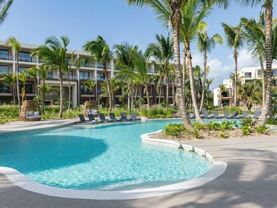 Modern hotel complex with a large, curved pool and palm trees outdoors.