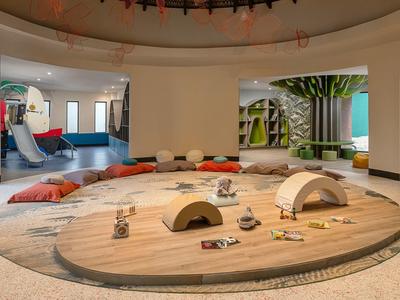 Moderner, offener Hotelbereich mit rundem Holztisch und bunten Sitzkissen.