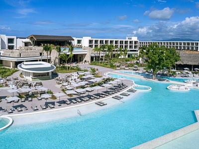 Luxuriöses Resort mit großen Pools, Liegestühlen und modernen Gebäuden unter blauem Himmel.