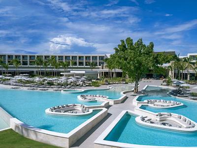 Modern hotel pool with islands and lounge chairs under a blue sky.