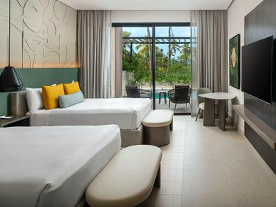 Modernes Hotelzimmer mit zwei Betten, Sitzgelegenheiten und Balkon mit Blick ins Grüne.