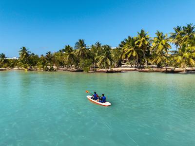 Zwei Personen paddeln auf einem Kajak in türkisfarbenem Wasser vor Palmenstrand.