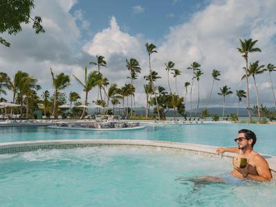 Ein Mann entspannt sich in einem Pool mit Palmen und einem bewölkten Himmel im Hintergrund.