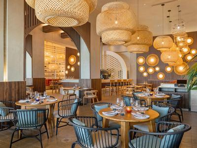 Ristorante moderno con tavoli rotondi in legno, sedie imbottite e luci calde a soffitto.
