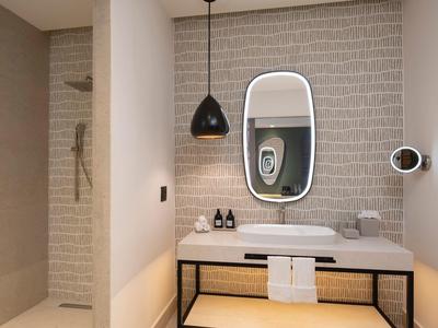 Modernes Badezimmer mit rechteckigem Spiegel, schwarzer Pendelleuchte und offener Dusche links.