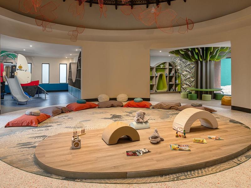 Moderner, offener Hotelbereich mit rundem Holztisch und bunten Sitzkissen.