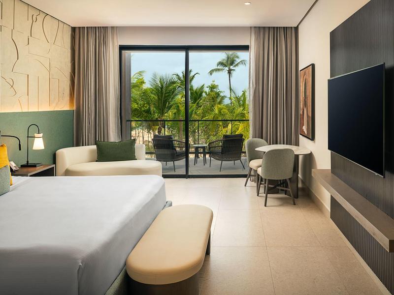 Helle Hotelzimmer mit großem Bett, Balkon und Blick auf Palmen