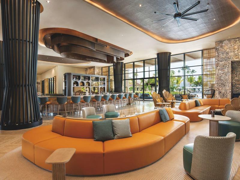 Moderner Hotel-Loungebereich mit geschwungener oranger Sofa, großen Fenstern und elegantem Design.