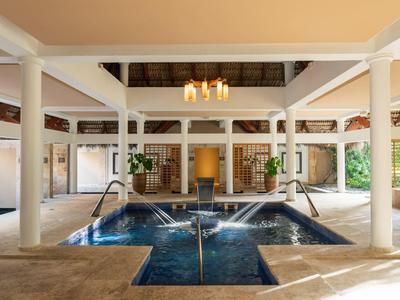 Indoor pool with modern water jets, surrounded by white columns and a thatched roof ceiling.