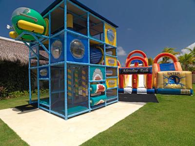 Outdoor children's play area with climbing structures and inflatable bounce houses on grass.