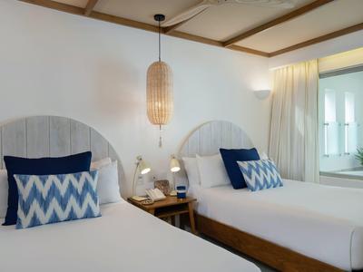 Hotel room with two single beds, patterned pillows, bedside lamps, and soft curtains.