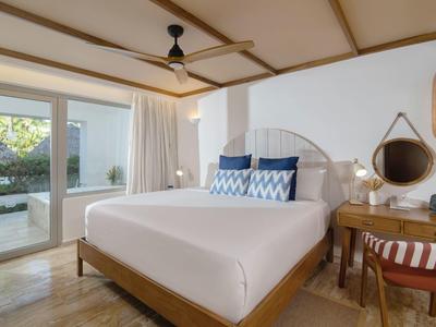 Cozy hotel room with large bed, wooden ceiling beams, sliding glass doors, and a garden view.