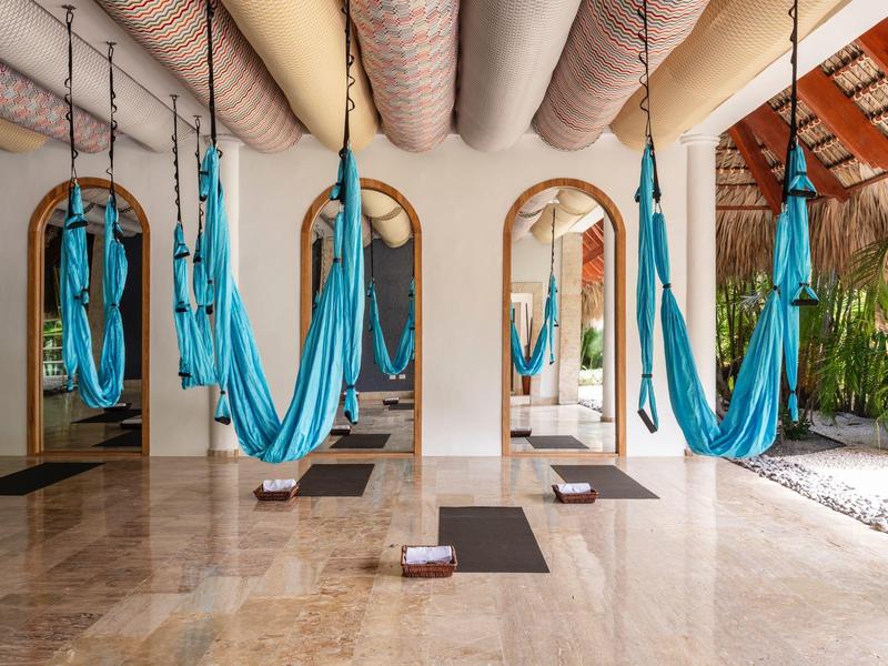 Spa room with blue hammocks, yoga mats, and wooden beams, reflecting in three arches.