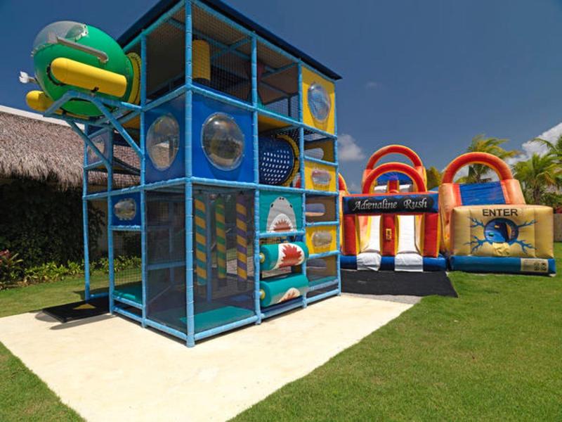 Outdoor children's play area with climbing structures and inflatable bounce houses on grass.