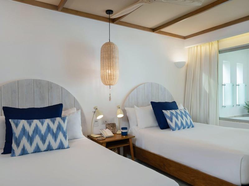 Hotel room with two single beds, patterned pillows, bedside lamps, and soft curtains.