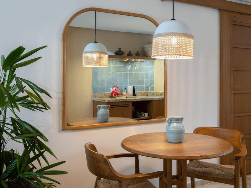Cozy dining area with a round wooden table, chairs, pendant lights, and a large mirror reflecting a kitchen.