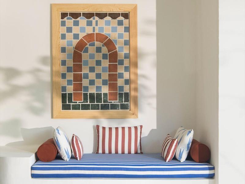 Cozy seating area with blue cushioned bench, striped pillows, wooden table, and colorful wall art.
