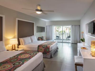 Helles Hotelzimmer mit zwei Betten, Deckenventilator, Terrassentür und modernem Kamin.