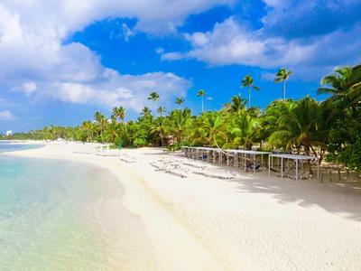 Weißer Sandstrand mit klarem Wasser, Palmen und blauem Himmel mit Wolken.