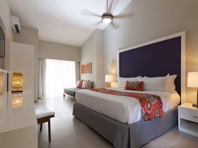 Helles Hotelzimmer mit großem Bett, Deckenventilator und Zugang zu Balkon mit Tageslicht.