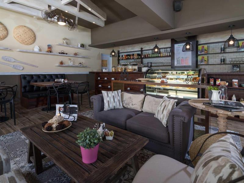 Gemütliches Café mit Holztischen, bequemen Sitzmöbeln, Pflanzen und dekorativer Wandgestaltung.