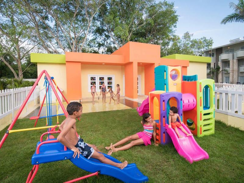 Kinder spielen auf buntem Spielplatz mit Rutsche, Schaukel und Klettergerüst im Garten.