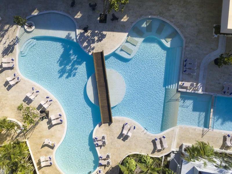 Großer, geschwungener Pool mit Sonnenliegen, Grünflächen und schattigen Bereichen, aus der Vogelperspektive.