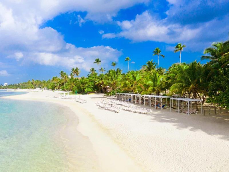 Weißer Sandstrand mit klarem Wasser, Palmen und blauem Himmel mit Wolken.