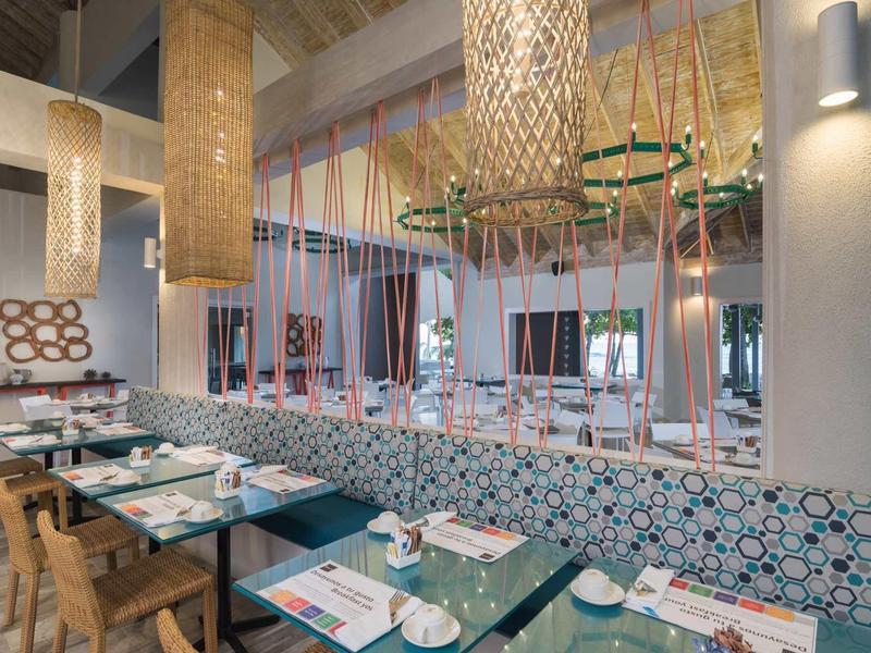 Modernes Restaurant mit bunter Dekoration, Holztischen und gemusterten Sitzbänken in warmem Licht.