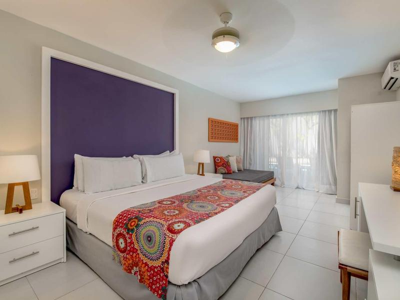 Modernes Hotelzimmer mit großem Bett, weißer Bettwäsche und lila Kopfteilstück.