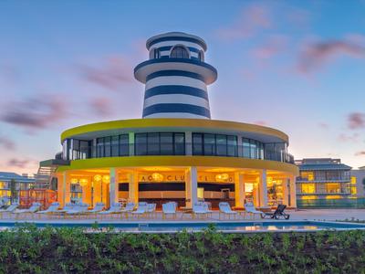 Modern hotel building with a round tower and illuminated ground floor at sunset.