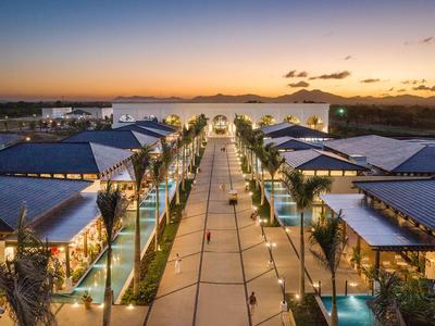 Lively shopping boulevard at sunset with modern stores and illuminated trees.