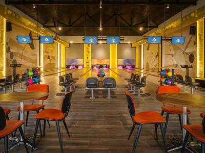 Innenansicht einer modernen Bowlingbahn mit Tischen und Stühlen im Vordergrund.