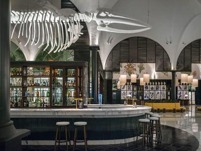 Eleganter Hotelbarbereich mit rundem Tresen, Barhockern und großem Skelett über der Bar